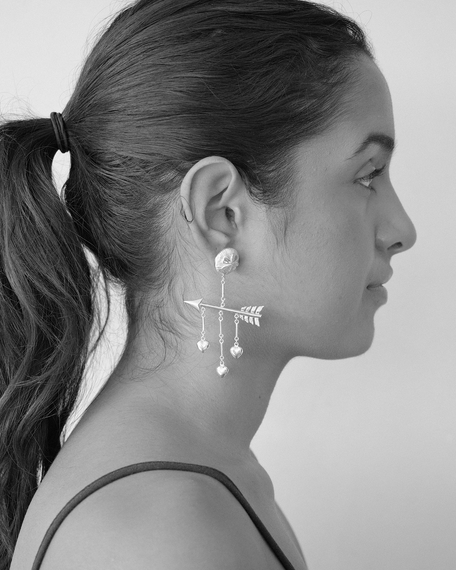 a model wears large drop earrings with an arrow, hearts and a clover stud