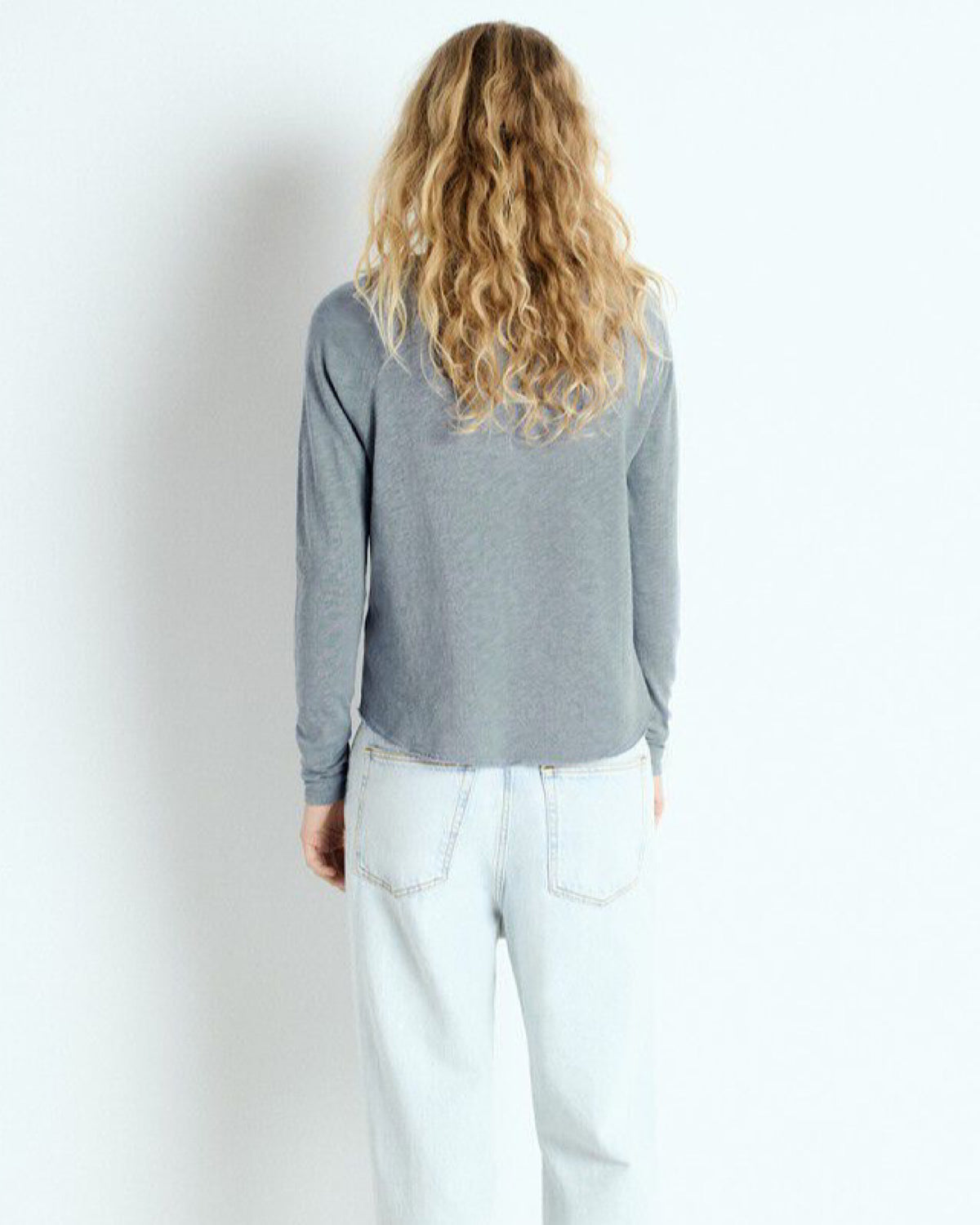 Person wearing a blue grey  long-sleeve shirt and light blue jeans against a white background