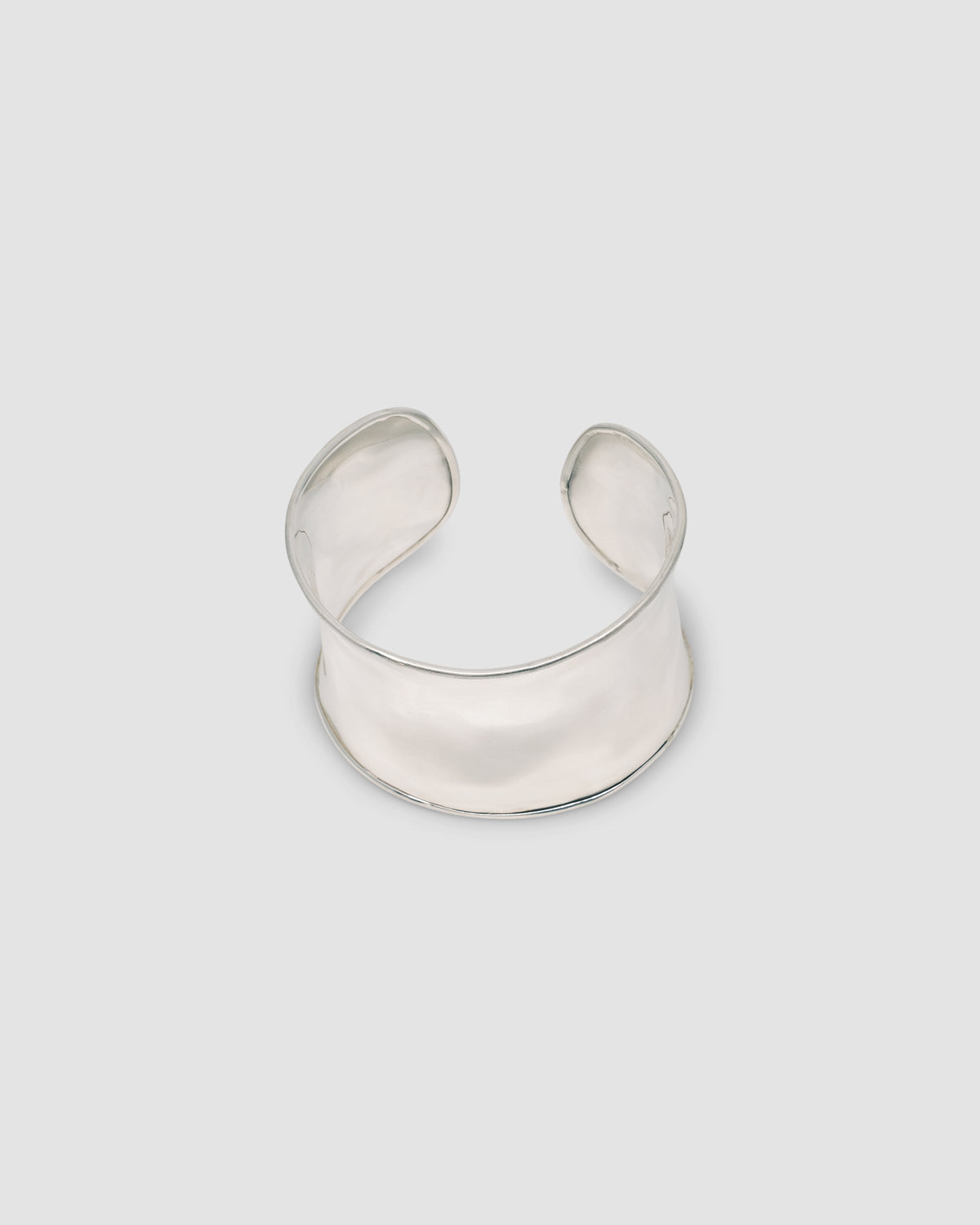 a super wide open sterling silver cuff bracelet sits on a marble plinth