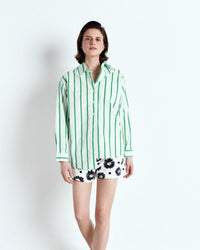 Woman wearing a green and white striped shirt with floral shorts on a white background