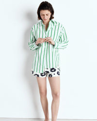 Woman wearing a green and white striped pajama set with black floral shorts on a white background