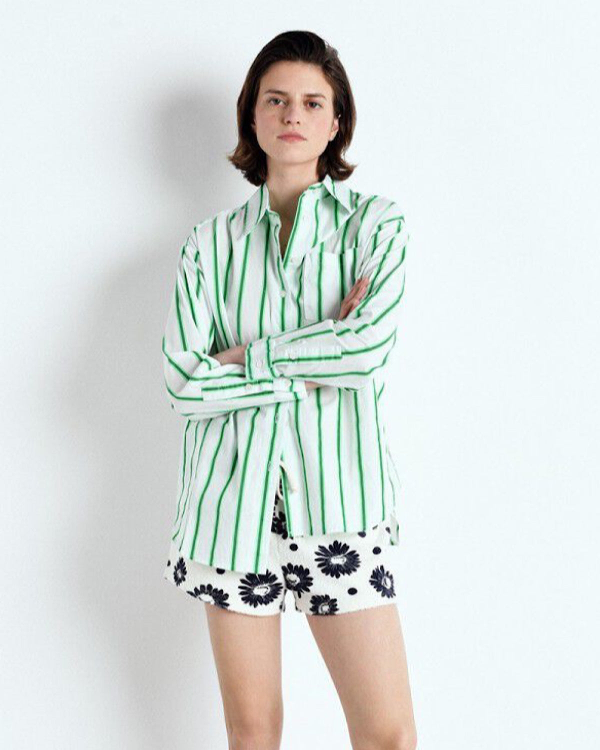 Person wearing a green and white striped shirt with floral shorts on a white background