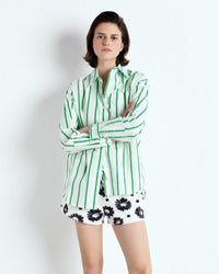 Person wearing a green and white striped shirt with floral shorts on a white background